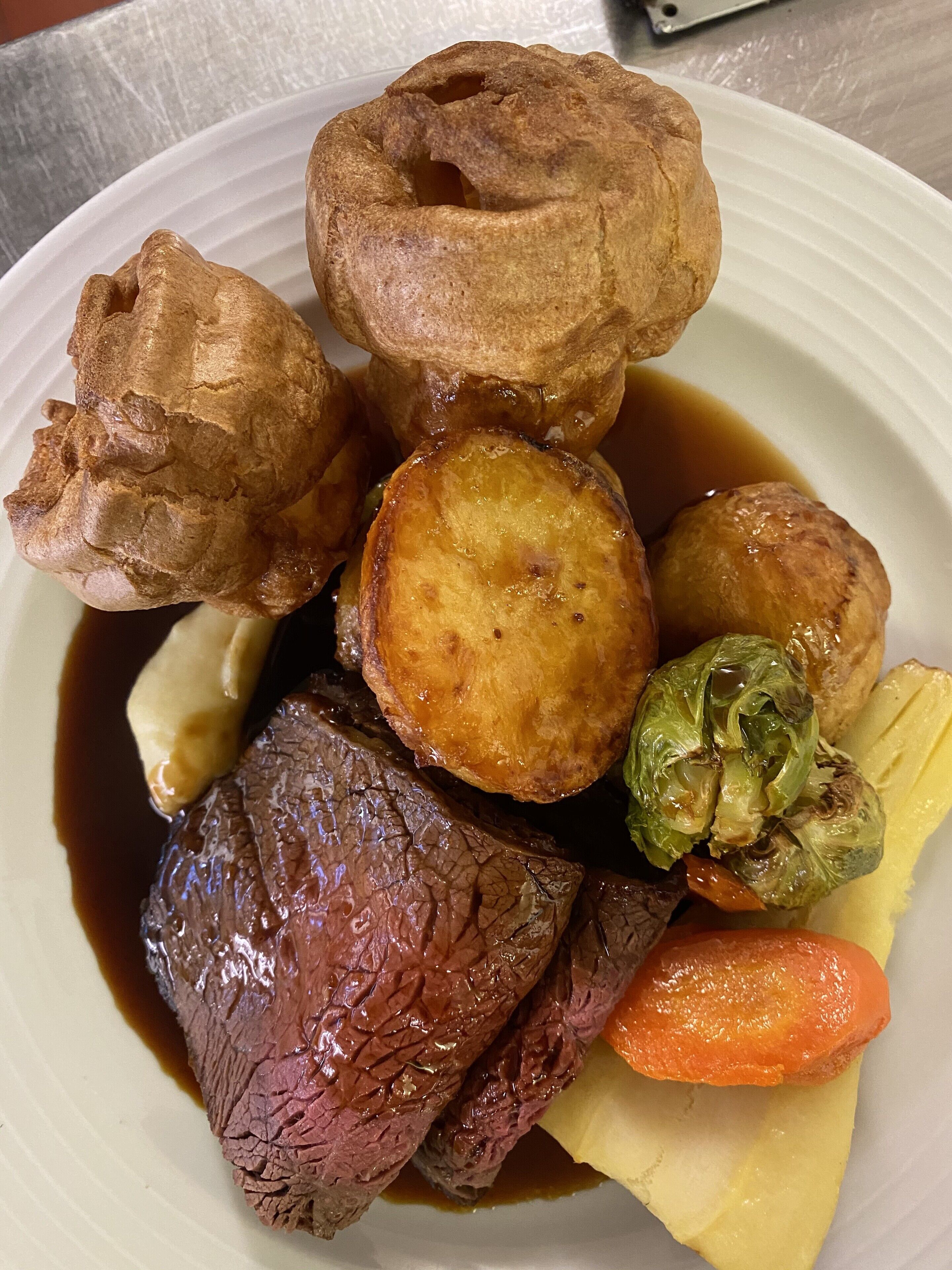 A plate of food including Yorkshire pudding, roast beef, carrots, and vegetables.