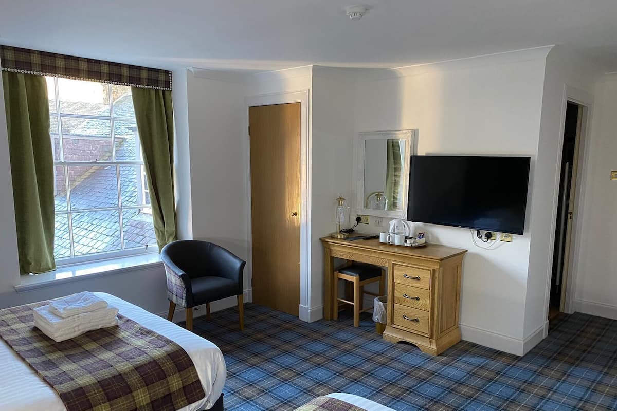 A hotel room with a bed, a desk with a chair, a television, and a window with curtains.