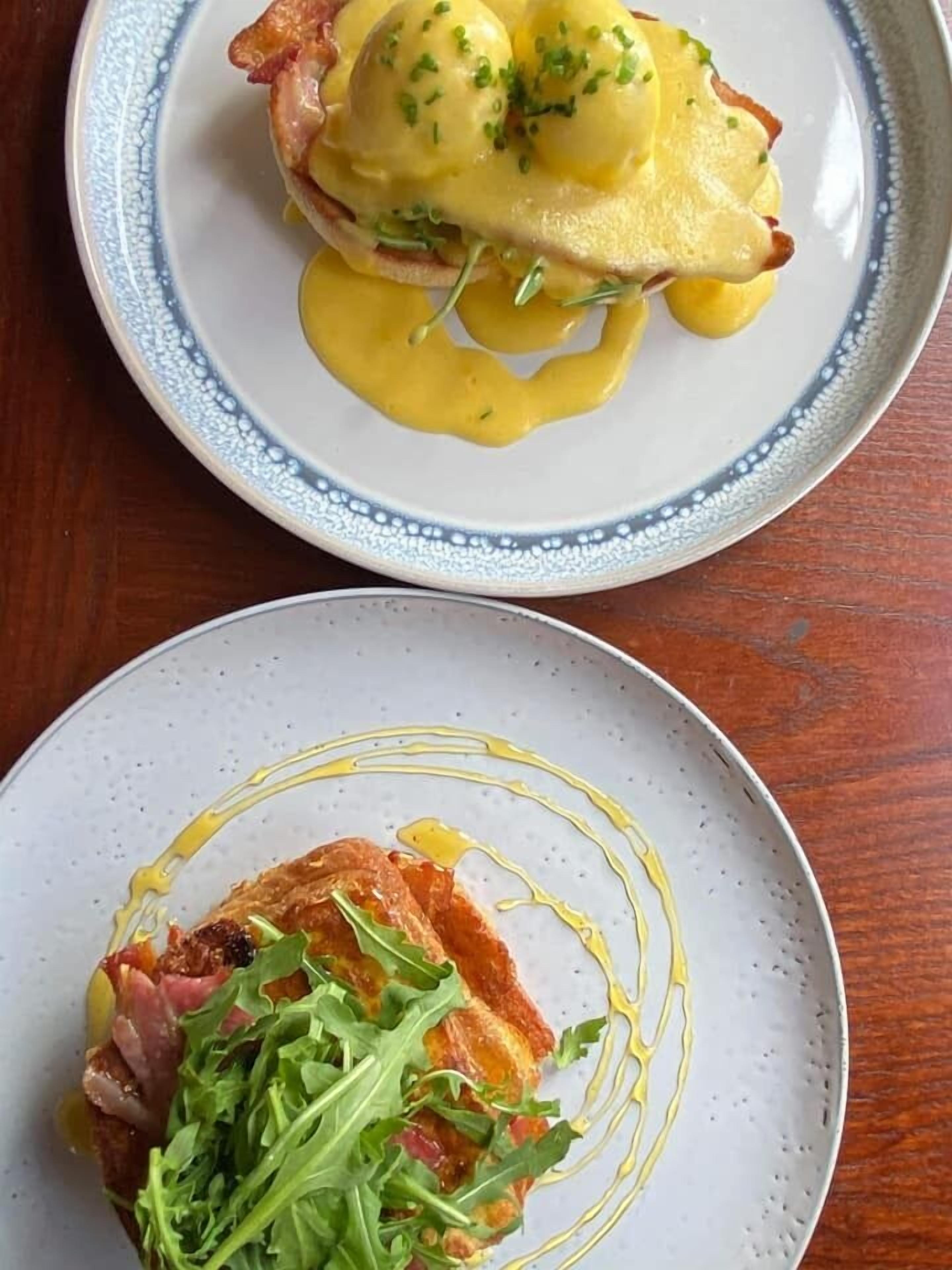 Dos platos de comida, uno con huevos Benedictinos y otro con un plato de carne y verduras.