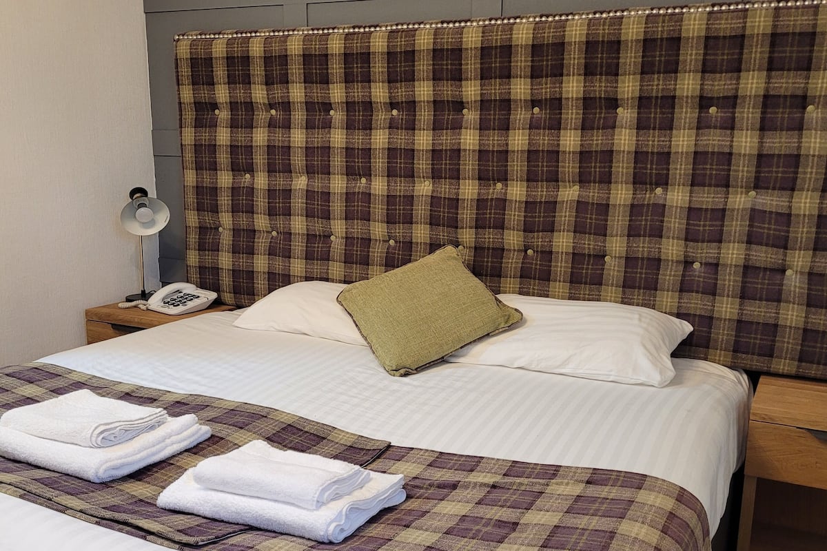 A neatly made bed with a plaid headboard, a bedside lamp, and folded towels on the bed.