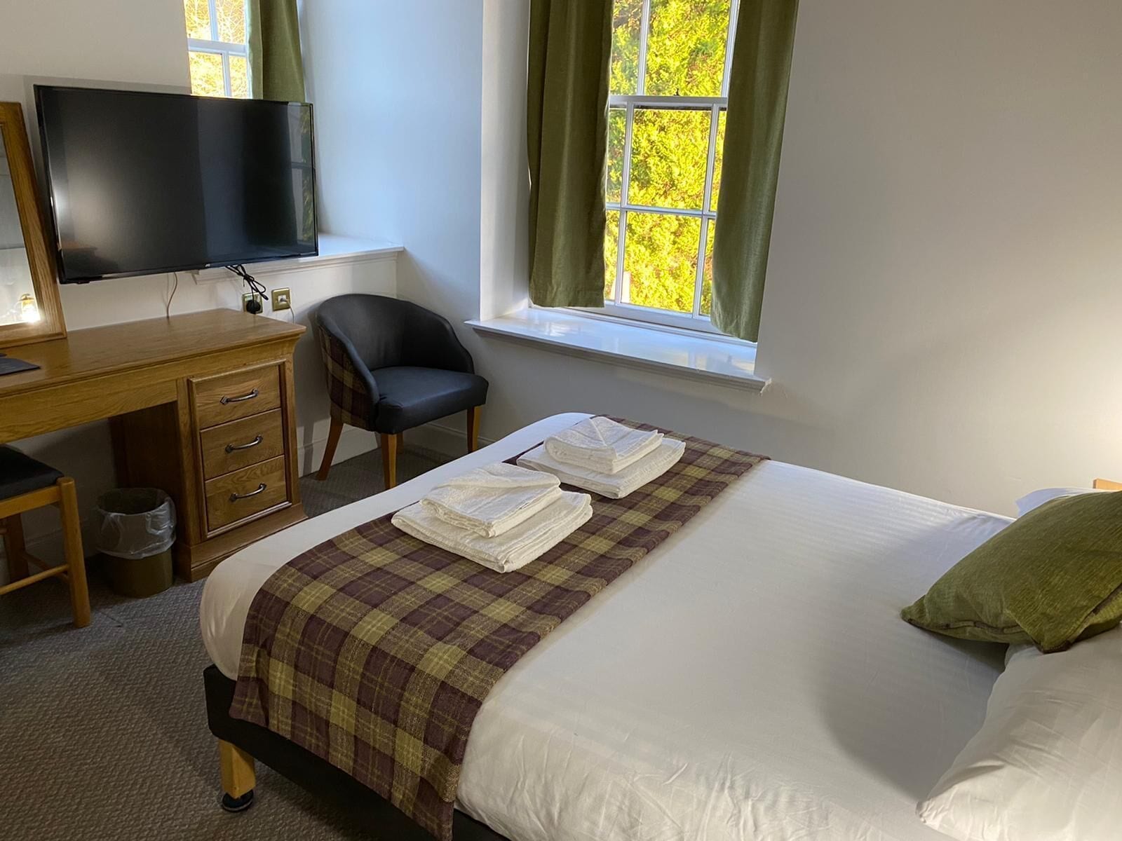 Ein Hotelzimmer mit einem Bett, einem Schreibtisch mit Fernseher, einem Stuhl und einem Fenster mit Vorhängen.