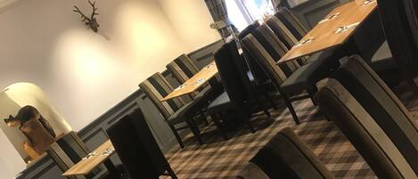 A dining area with checkered flooring, dark upholstered chairs, and a wooden table.