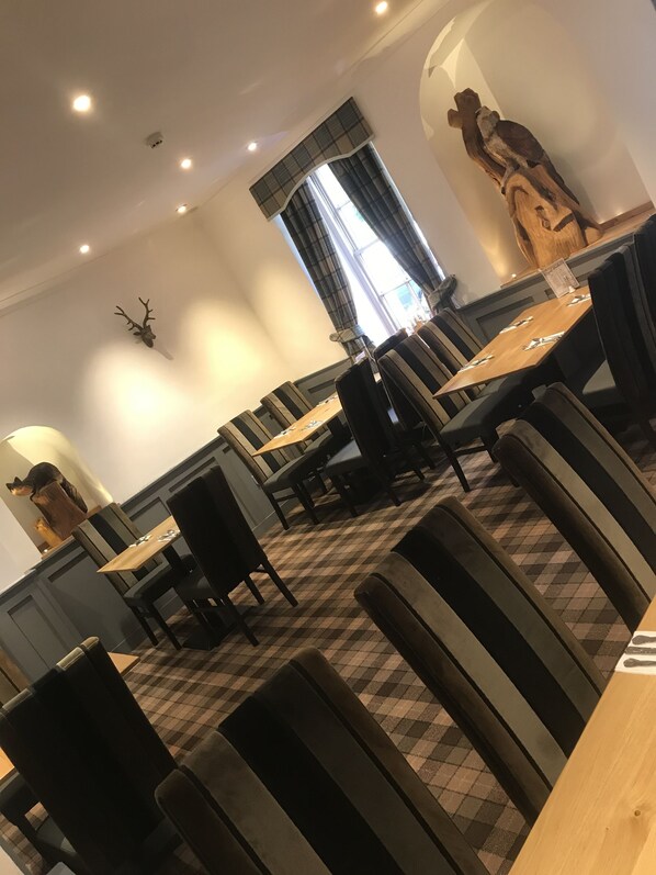 A dining area with checkered flooring, dark upholstered chairs, and a wooden table.