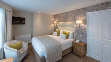 A hotel room with a large bed, bedside lamps, a chair, a bedside table with a phone, and a TV on the wall.
