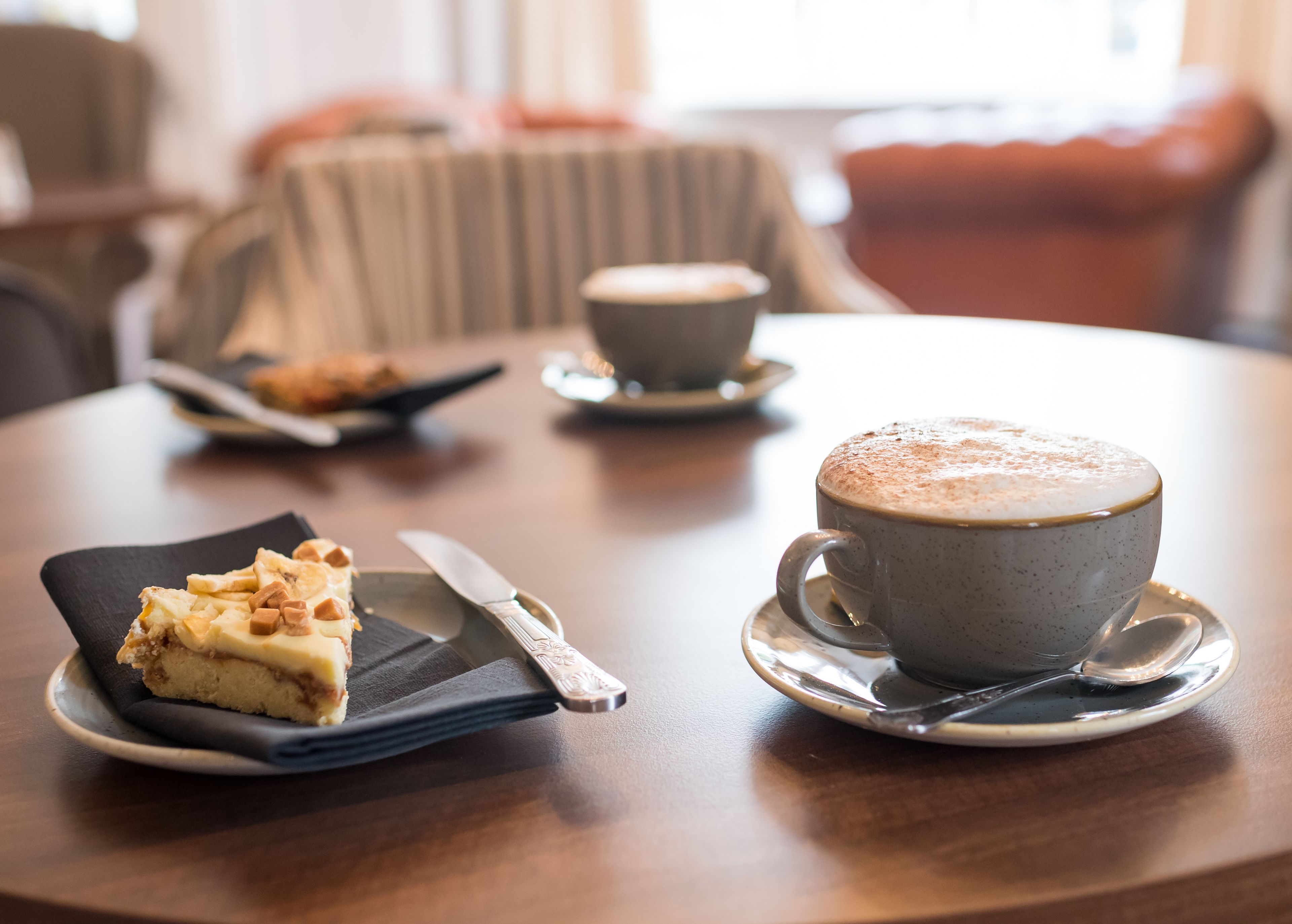 Una mesa con una porción de pastel, una taza de café y una cuchara.