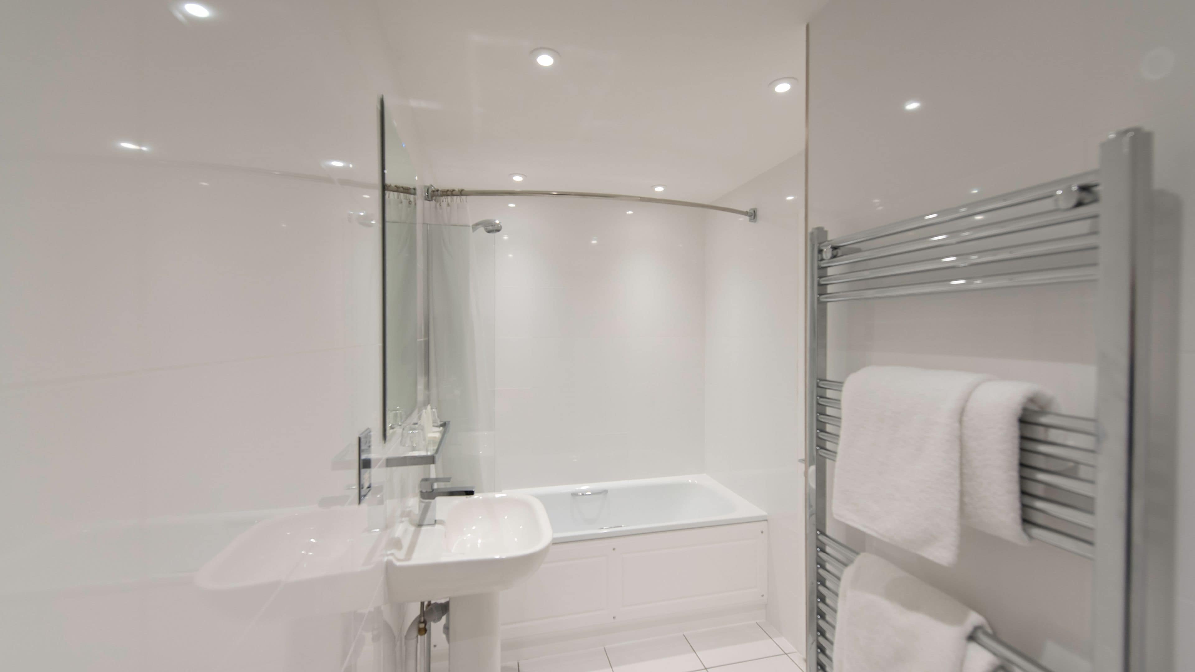 A modern bathroom with a glass shower enclosure, a white sink, and a towel rack.