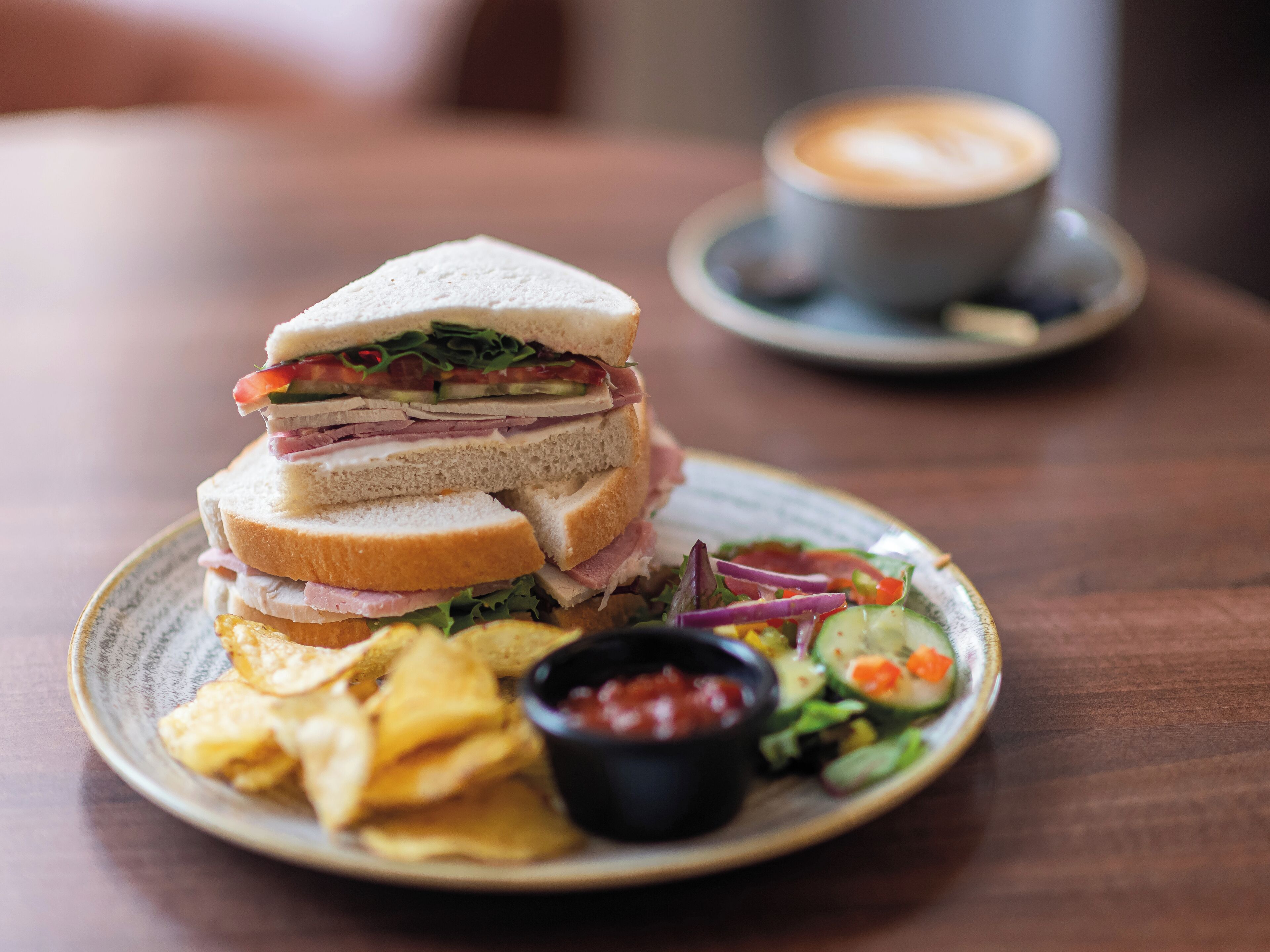 A plate with a sandwich, chips, a salad, and a cup of coffee on a wooden table.