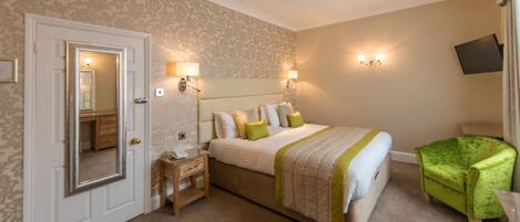 A hotel room with a large bed, bedside lamps, a television, and a green armchair.