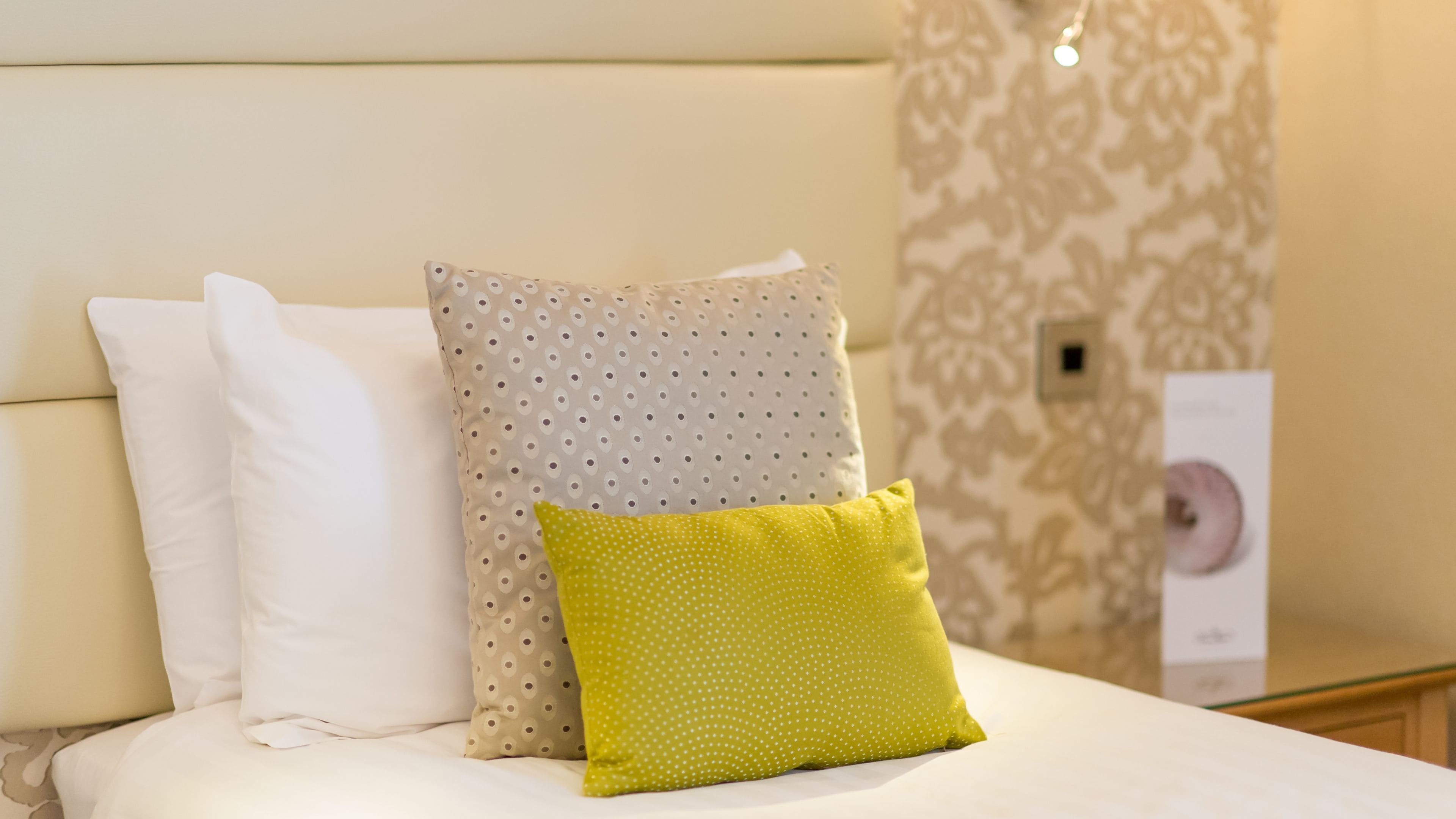 Ein Bett mit weißen und gemusterten Kissen, ein gelbes Kissen und eine Wand mit Muster im Hintergrund.