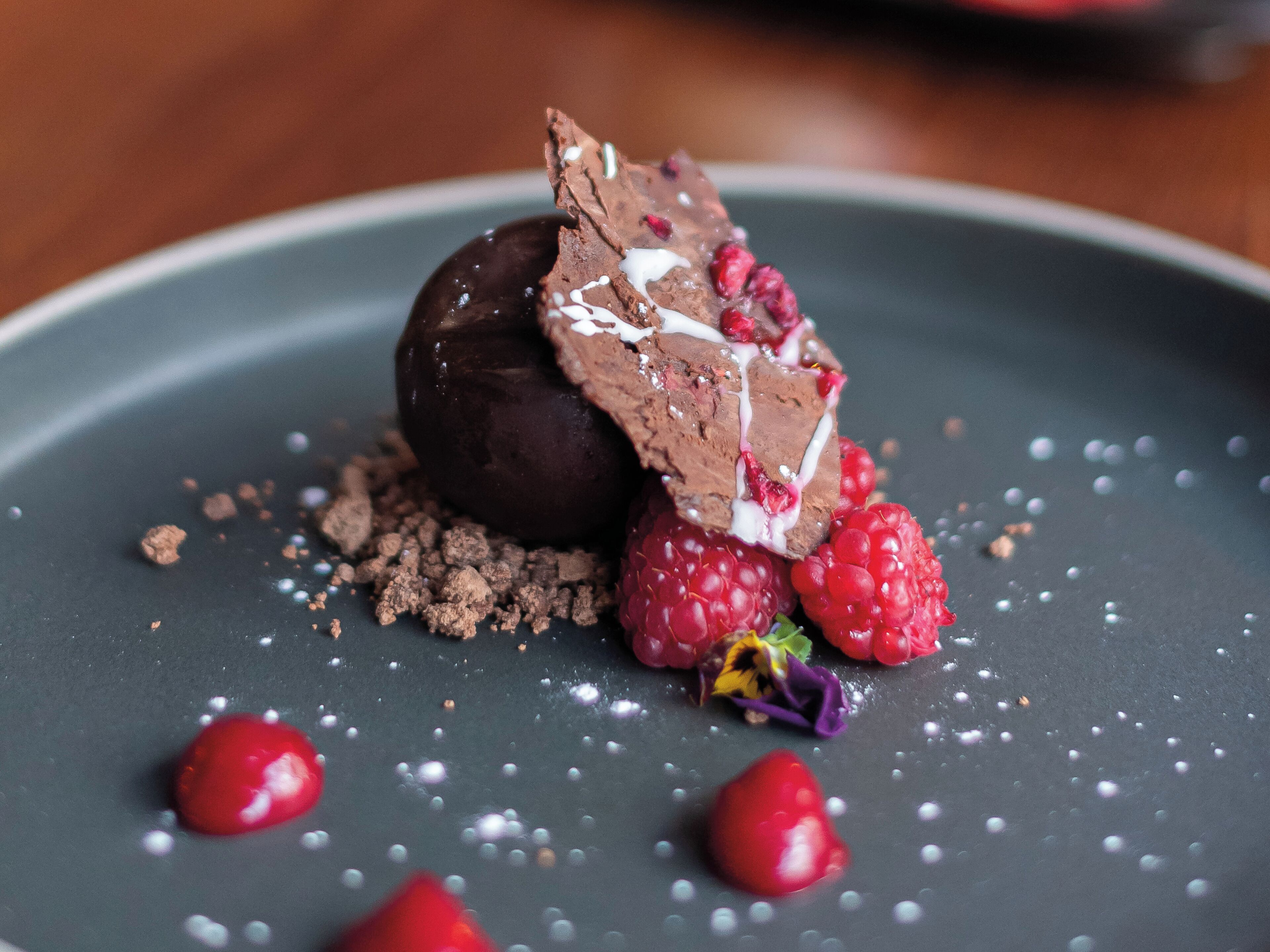 Un dessert à base de chocolat, de framboises et agrémenté d’un élément décoratif sur une assiette.