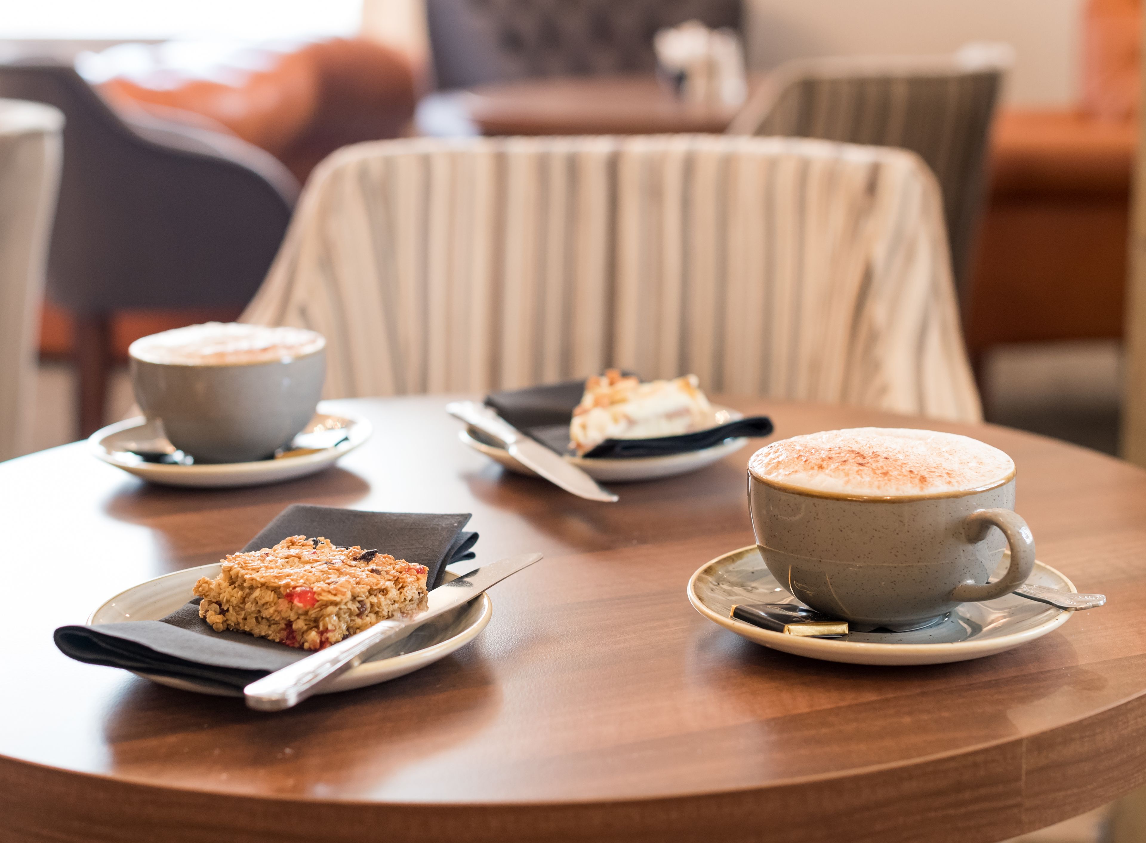 A round wooden table with three plates of food and two cups of coffee.