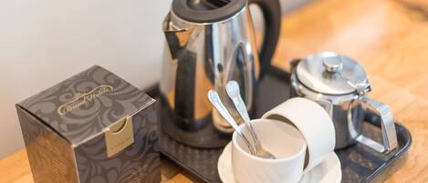 A coffee maker, a cup with a spoon, and a box on a tray.