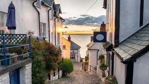 A cobblestone street in a coastal town with white buildings, a view of the sea, and hanging flower baskets. - The Royal & Fortescue (Barnstaple)