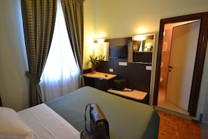 Una habitación de hotel con una cama, un escritorio con una silla, un televisor, un espejo y una puerta que da a un baño.