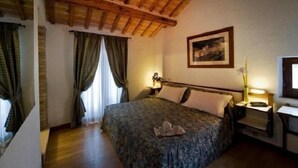 A bedroom with a wooden ceiling, a bed with a floral bedspread, a nightstand with a lamp, and a framed picture on the wall. - Hotel il Castello (Assisi)