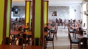 A restaurant with multiple tables and chairs, stone walls, and a television mounted on the wall. - Hotel il Castello (Assisi)