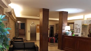 A lobby with a reception desk, a staircase, and seating area with a glass coffee table. - Hotel il Castello (Assisi)