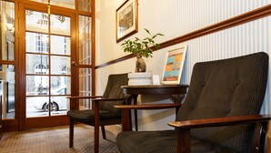 A room with two dark-colored chairs, a small table with a plant, and a framed picture on the wall. - Regency House (London)