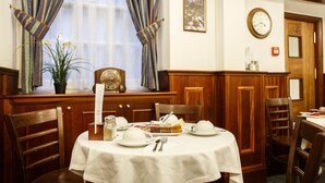 A dining area with a round table set for two, a clock on the wall, and a window with curtains. - Regency House (London)