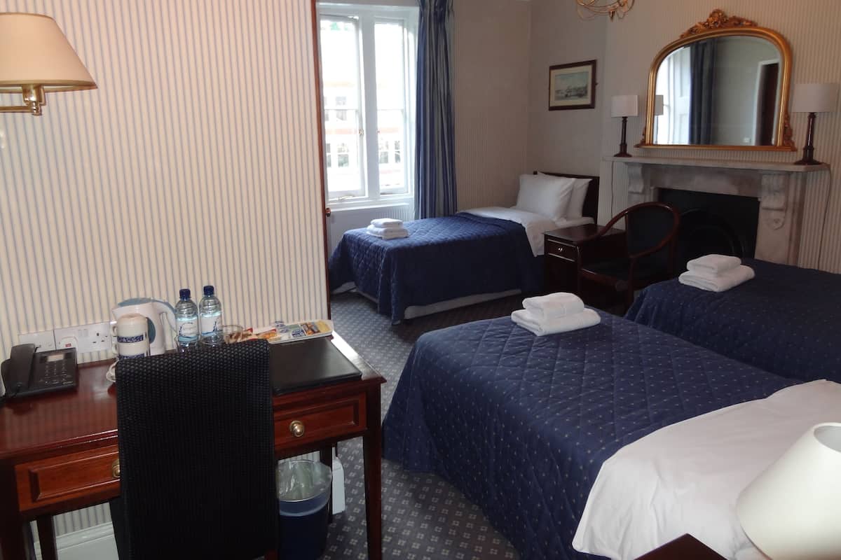 A hotel room with two beds, a desk with a telephone, a chair, a mirror, and a fireplace.