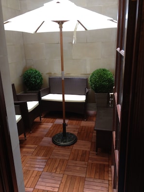 Un espace patio aménagé avec un canapé en osier, deux fauteuils, une petite table, une lampe sur pied et deux plantes en pot.
