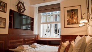 A hotel room with a bed, a television, a window with a view, and a ship's wheel decoration. - Regency House (London)