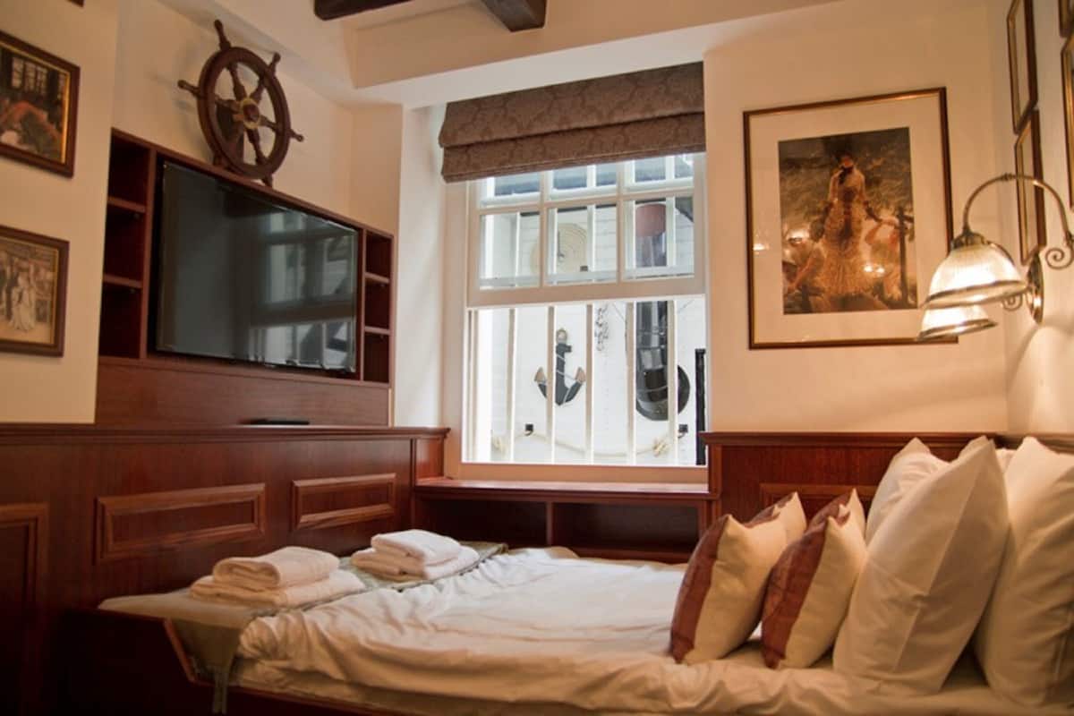 A hotel room with a bed, a television, a window with a view, and a ship's wheel decoration.