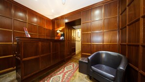 A lobby with wooden paneling, a reception desk, a leather sofa, and a patterned rug. - Regency House (London)