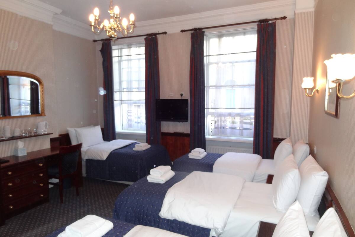 A hotel room with two beds, a desk, a chair, a TV, and a chandelier.