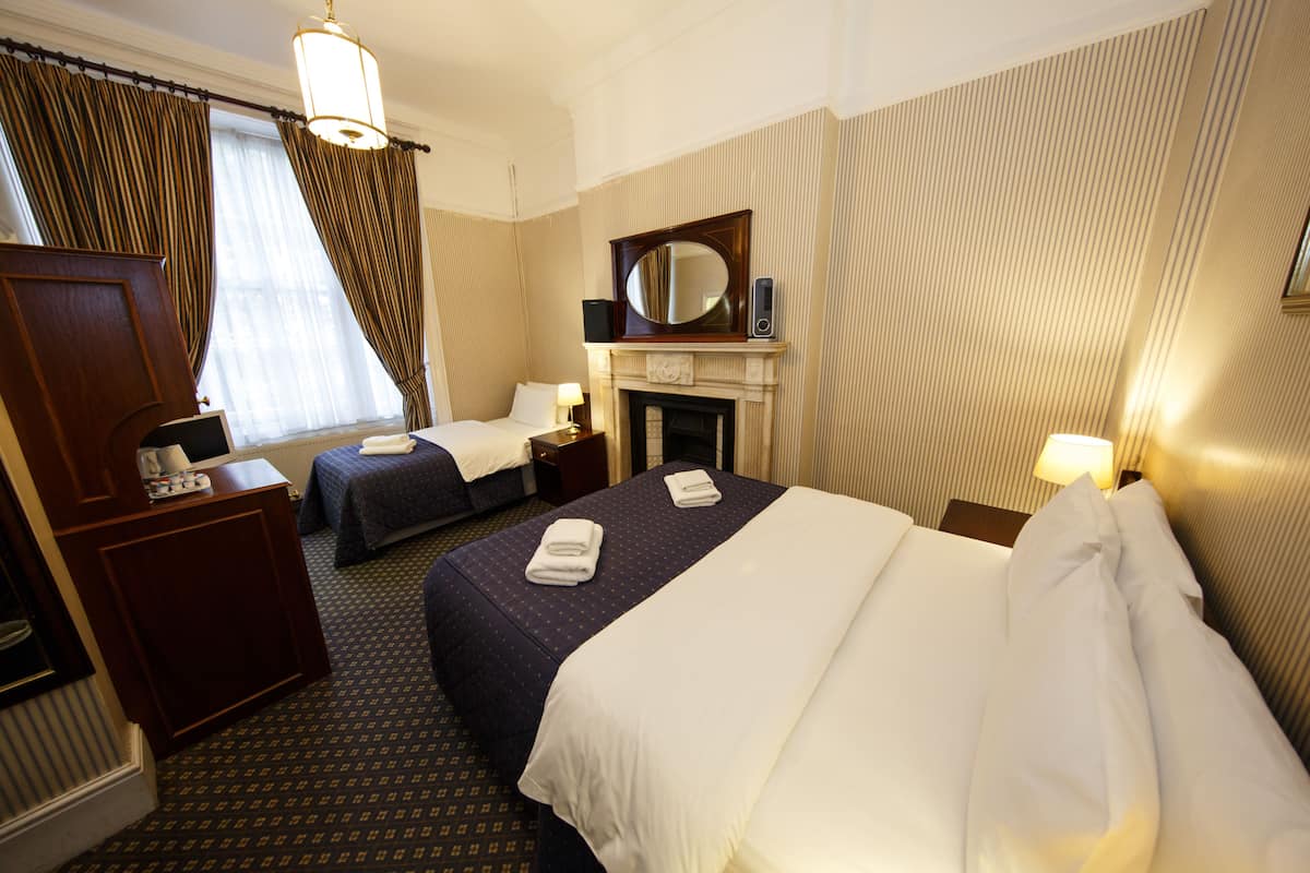A hotel room with two beds, a desk, a dresser, a fireplace, and a large mirror.