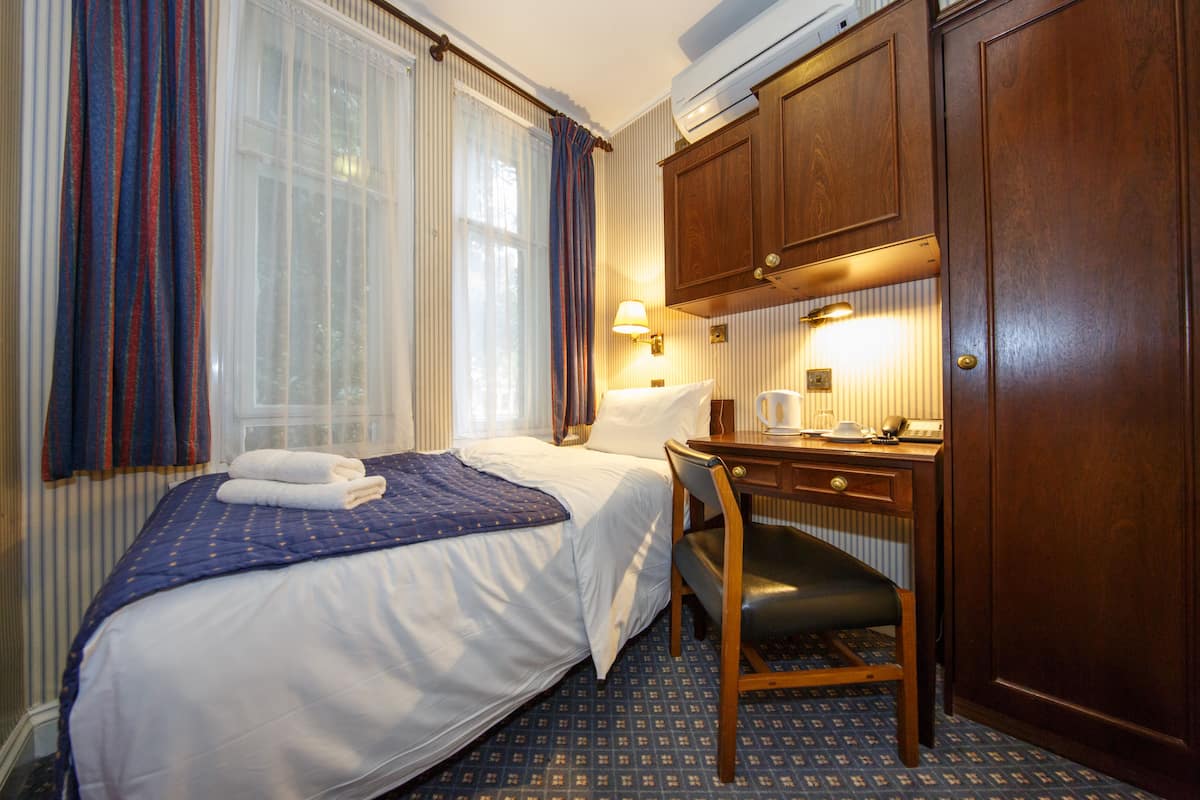 A hotel room with a bed, a desk, a chair, a lamp, and a wardrobe.