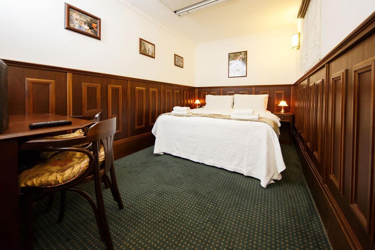 A hotel room with a bed, a desk with a chair, and a lamp.