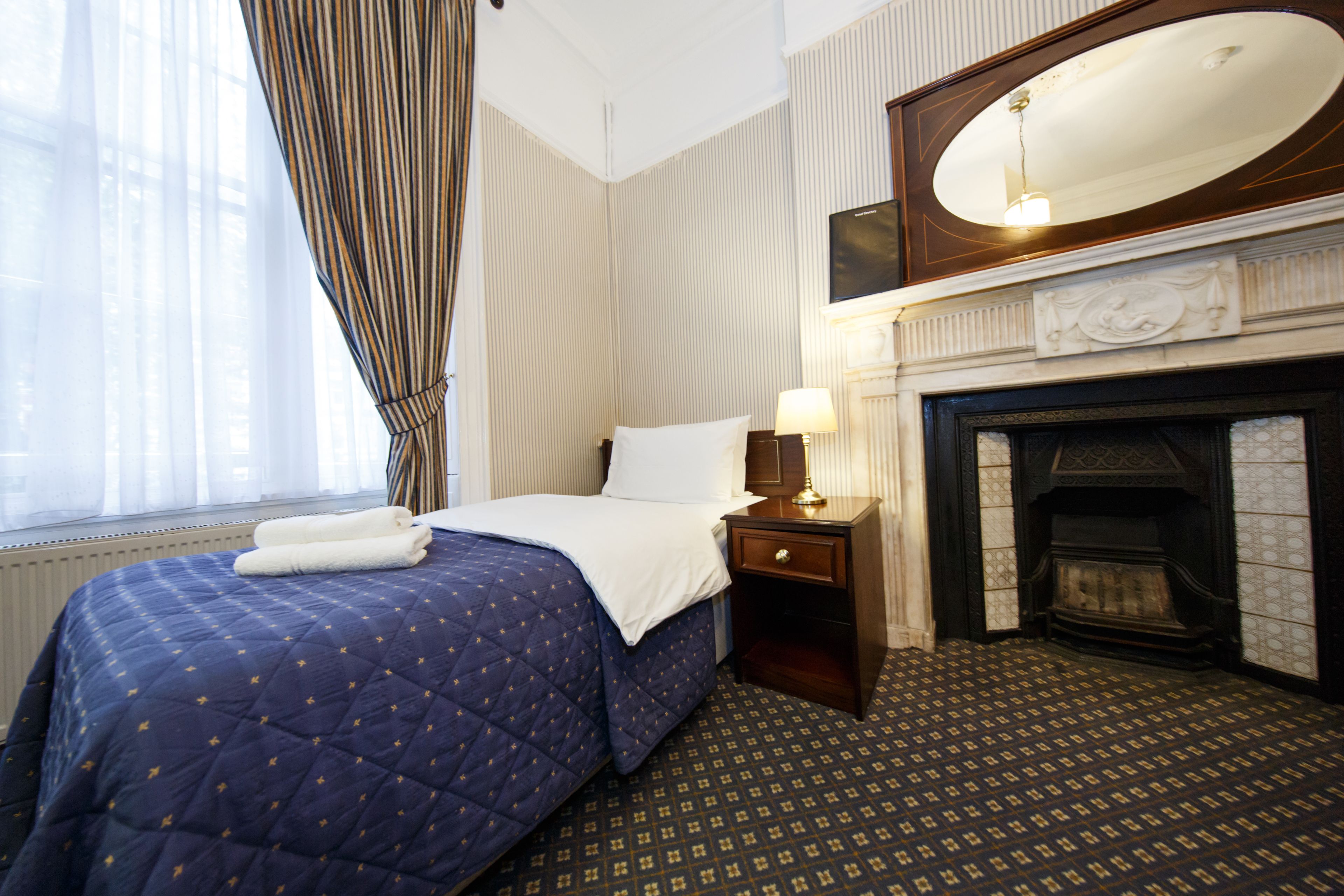 Habitación de hotel con cama, mesita de noche, lámpara, chimenea y un espejo grande.