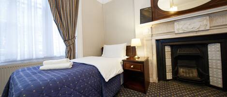 Habitación de hotel con cama, mesita de noche, lámpara, chimenea y un espejo grande.