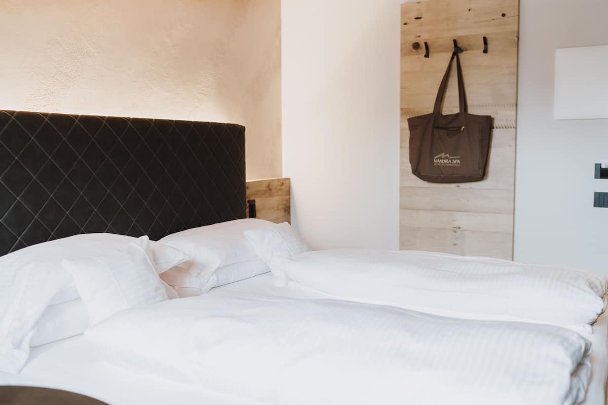 Una cama bien hecha con sábanas blancas, un cabecero oscuro y una pared de madera con un bolso colgando.