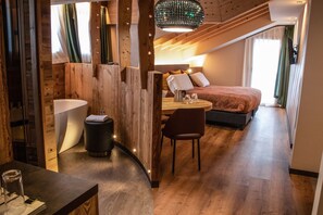A modern hotel room with a wooden interior, a round dining table, a bed, and a bathroom with a bathtub. - Hotel Concordia (Livigno)
