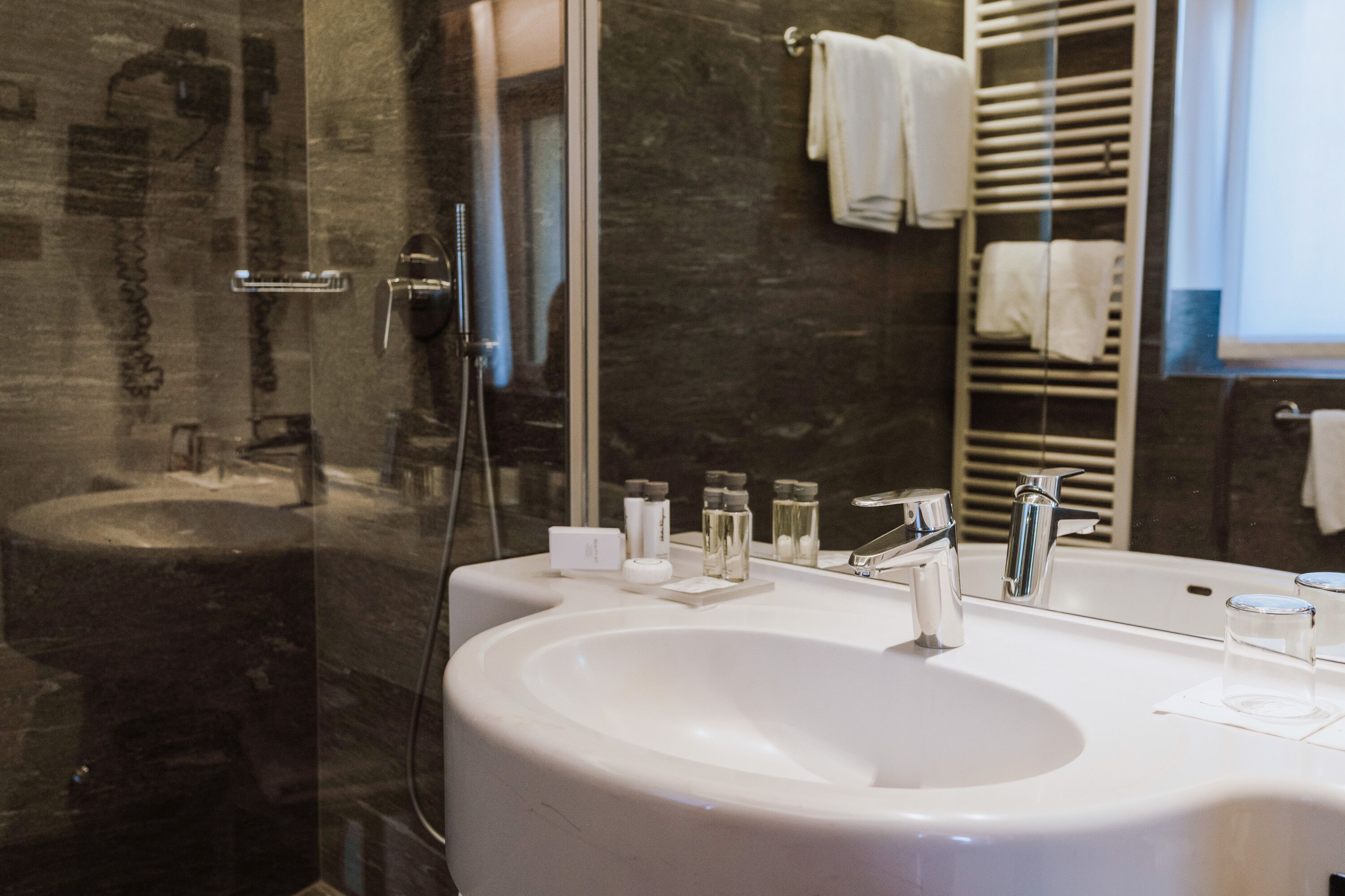 Un baño moderno con un lavamanos grande de color blanco, una mampara de ducha de vidrio y un perchero para toallas.