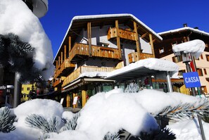 Un edificio de madera de varios pisos con balcones, un letrero que dice "CASSA" y alrededores cubiertos de nieve.