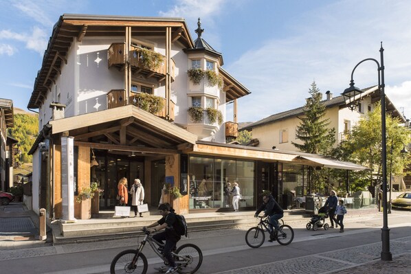 Un edificio con balcón, escaparate y una calle con gente y bicicletas.