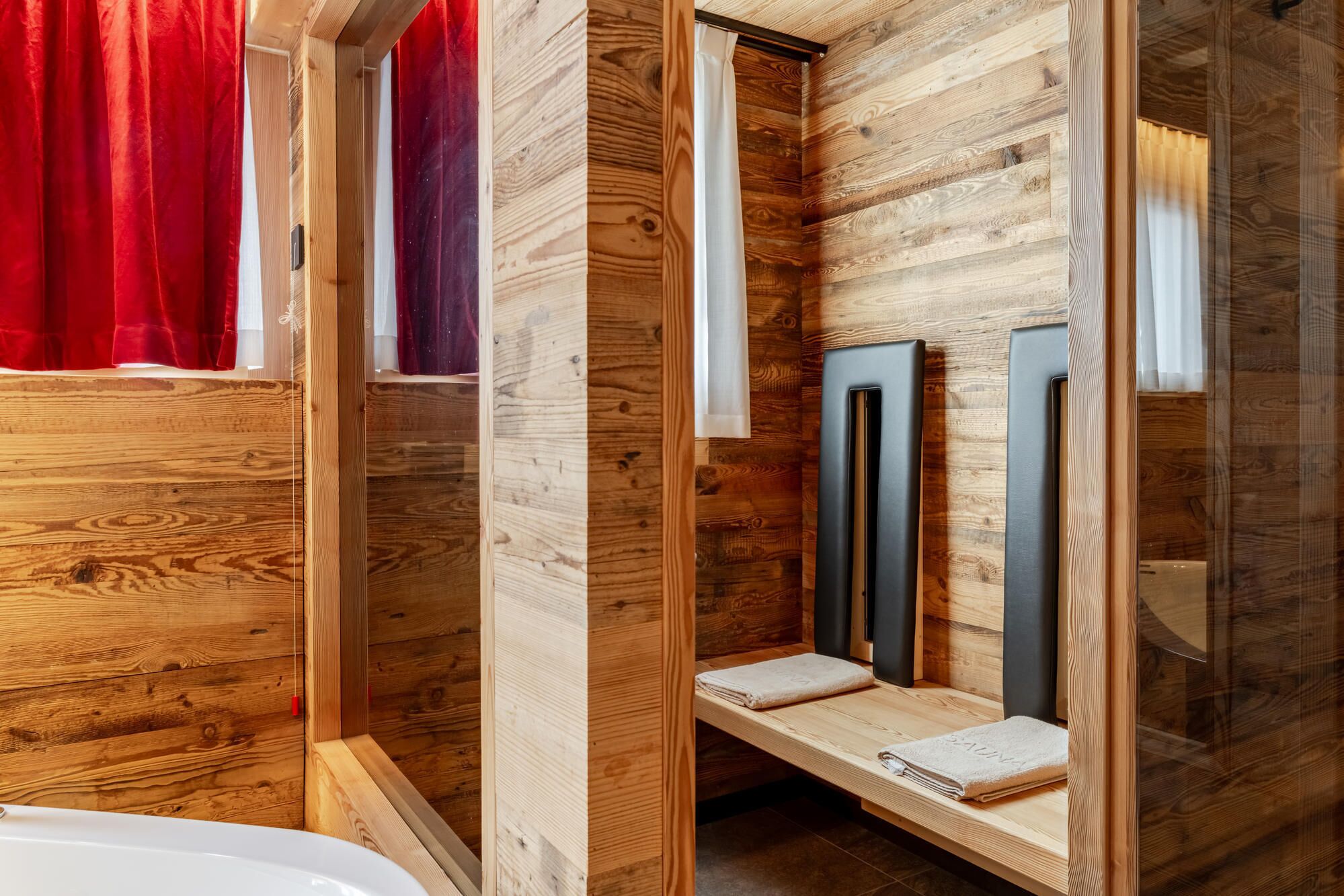 A wooden bathroom with a bathtub, a shower area, and a vanity with a mirror.