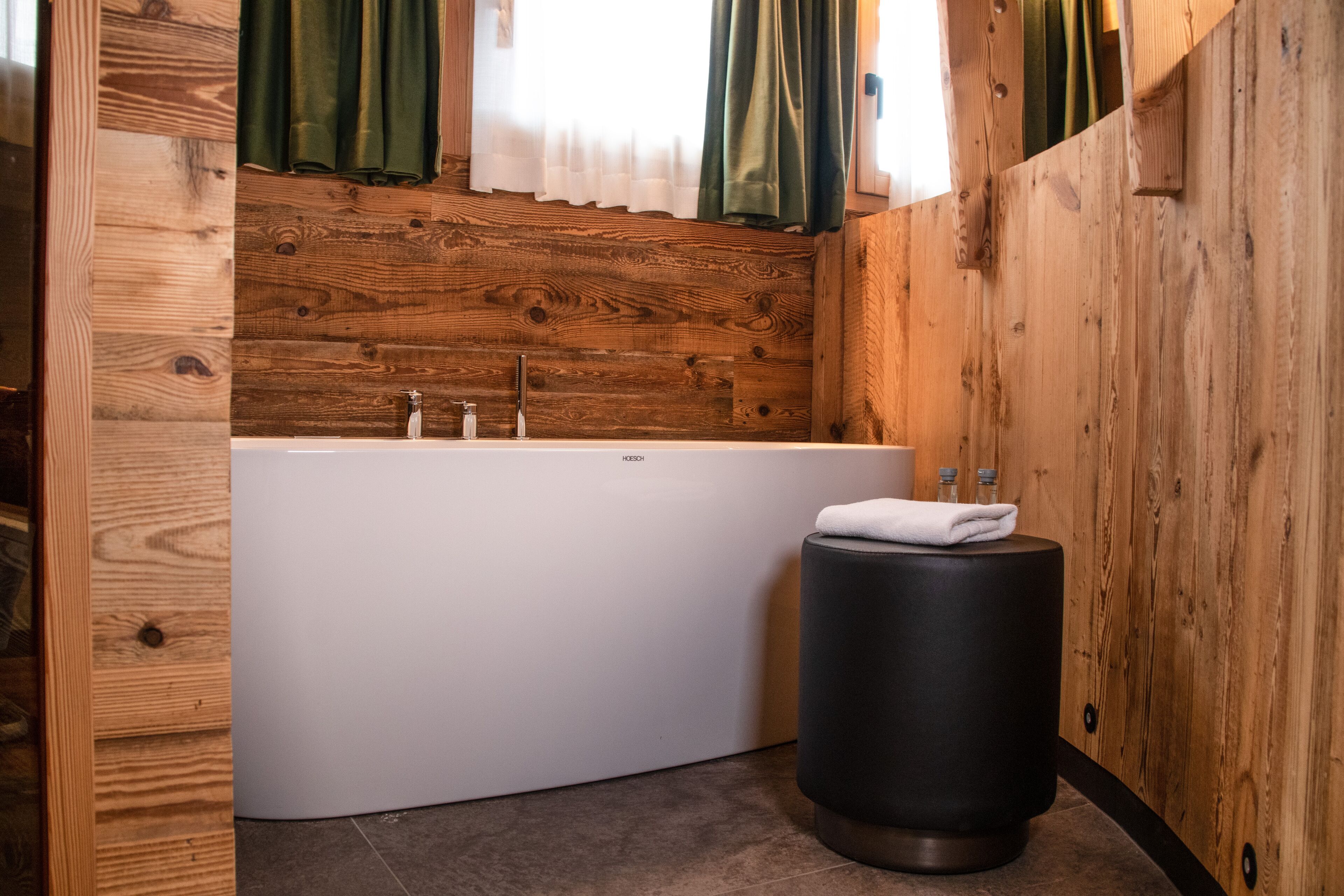 A modern bathroom with a wooden wall panel, a white bathtub, and a black waste basket.