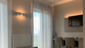 Habitación de hotel con una cama grande, un escritorio con dos sillas, un ventilador de techo y un televisor montado en la pared.