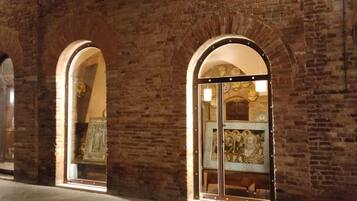 Un edificio ad arco in mattoni con ingresso tramite porta in vetro, illuminato da luci esterne.