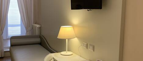 Une chambre d’hôtel avec un lit, un bureau avec une lampe, un téléviseur fixé au mur et une fenêtre avec des rideaux.