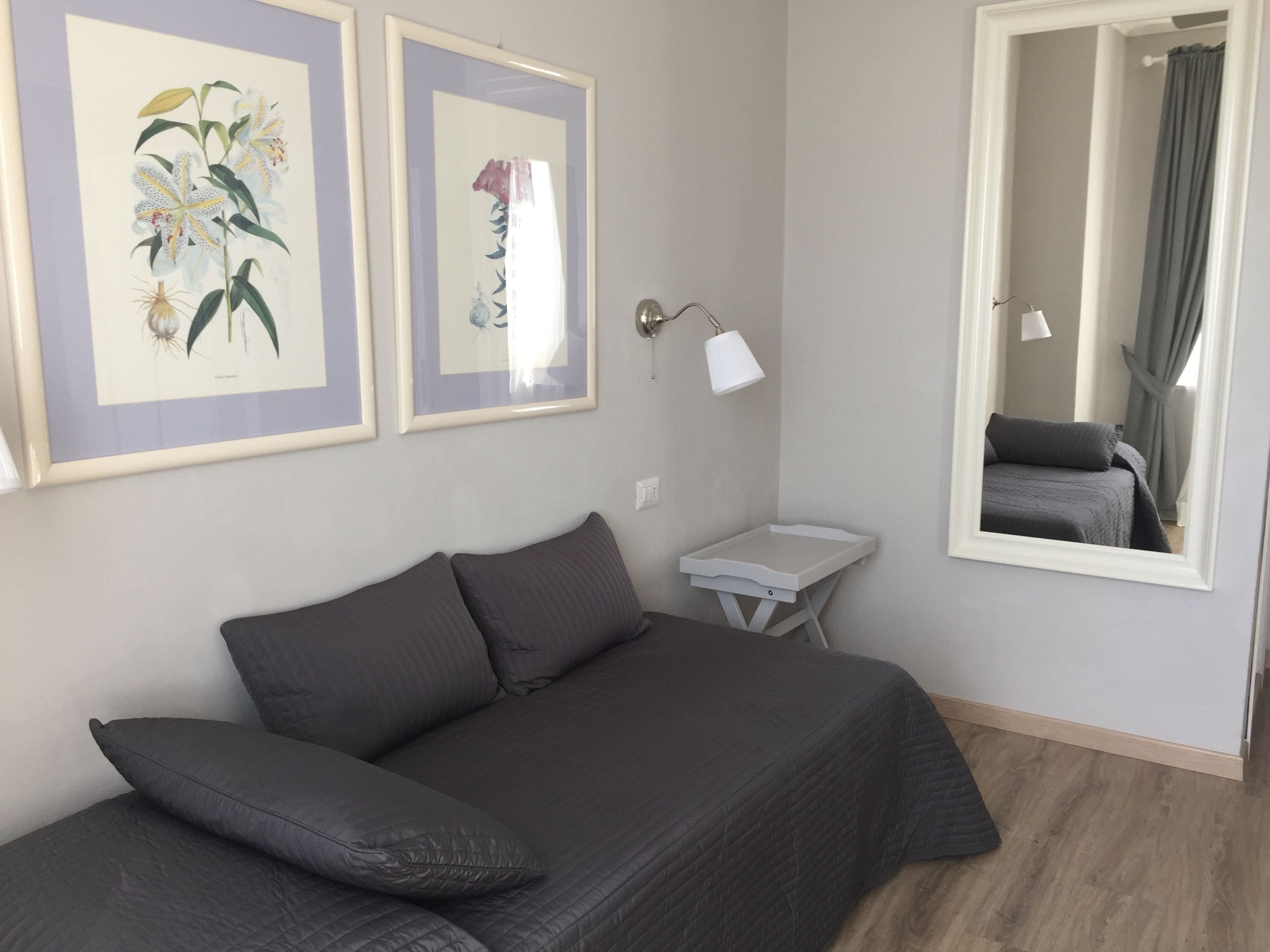 Un dormitorio con una cama, una mesita de noche, una lámpara y dos láminas enmarcadas con motivos botánicos en la pared.