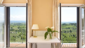 Un balcón con una mesa, una lámpara y un jarrón de flores, con vistas a un paisaje pintoresco.