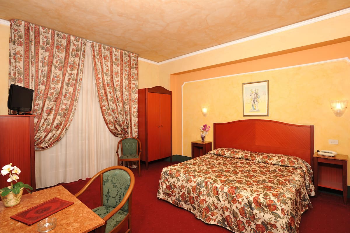 A hotel room with a bed, a desk with a chair, a television, and a window with curtains.