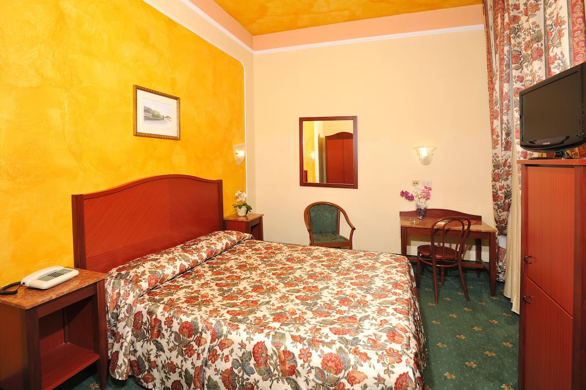 A hotel room with a bed, a desk, a chair, a television, and a telephone.