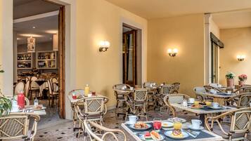 Um café ao ar livre com móveis de vime, mesas montadas para o pequeno-almoço e vista para o interior do restaurante.