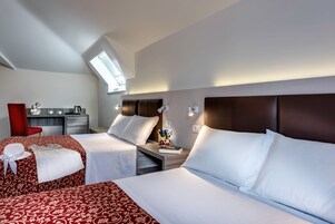 A hotel room with two beds, a desk, a red chair, and a skylight.